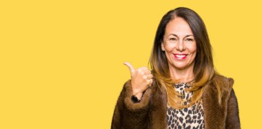 Seyir ve başparmak yanında yukarıyı mutlu yüz ile gülümseyen vizon kürk giyen güzel orta yaş zarif kadın.