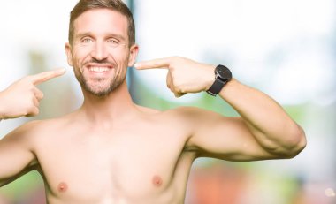 Gömleksiz yakışıklı gösteren çıplak göğüs emin gösterilen ve işaret parmakları diş ve ağız ile gülümseyen. Sağlık kavramı.