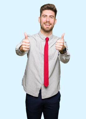 Genç yakışıklı iş adamı el ile pozitif jest yapıyor onaylama başparmak gülümseyen ve başarı için mutlu. Kamera, kazanan jest arıyorsunuz.