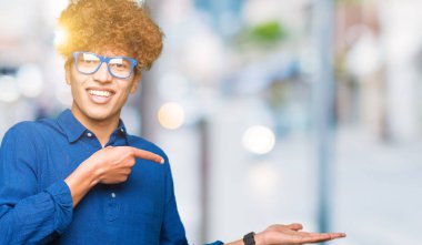 Hayret ve el ile sunulması ve parmak ile işaret ederken kameraya gülümseyen mavi gözlük takan afro saçlı genç yakışıklı adam.
