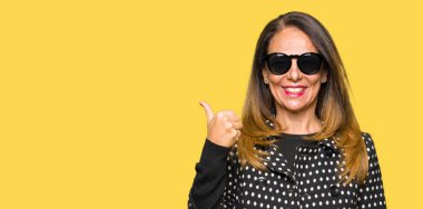 Seyir ve başparmak yanında yukarıyı mutlu yüz ile gülümseyen güneş gözlüğü takıyor güzel orta yaş kadın.