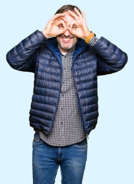 Orta yaş yakışıklı adam, dilini parmaklarının arasından baktığını yapışmasını dürbün gibi ok jest yapıyor kış palto giyiyor. Deli ifade.