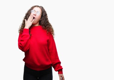 Güzel esmer kıvırcık saçlı esneme izole arka plan üzerinde gözlük ve kış kazak giyen genç kız sıkılmış kapsayan ağız el ile yorgun. Restless ve uyku hali.