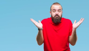 Üzerinde kırmızı gömlek giyen genç beyaz hipster adam arka plan clueless ve şaşkın bir ifadeyle kollar ve eller kaldırdı izole. Şüphe kavramı.