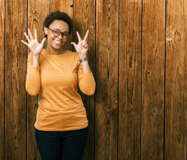 Genç güzel Afrikalı-Amerikalı kadın gözlük gösterilen ve parmakları ile işaret izole arka plan üzerinde kendinden emin ve mutlu gülümseyerek süre sekiz numara.