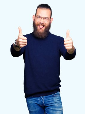 Gözlük ve el ile pozitif jest yapıyor onaylama boğazlı kazak giyen genç sarışın adam başparmak gülümseyen ve başarı için mutlu. Kamera, kazanan jest arıyorsunuz.