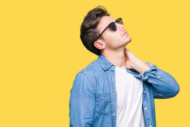 Genç yakışıklı adam giyen güneş gözlüğü izole üzerinde elle, kas ağrısı boyun dokunmadan acı boyun ağrısı yaralanma, arka plan