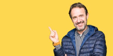 Kameraya bakarak yan el ve parmak ile işaret yüzünde, kocaman bir gülümseme ile kış ceket giyen orta yaş yakışıklı adam.