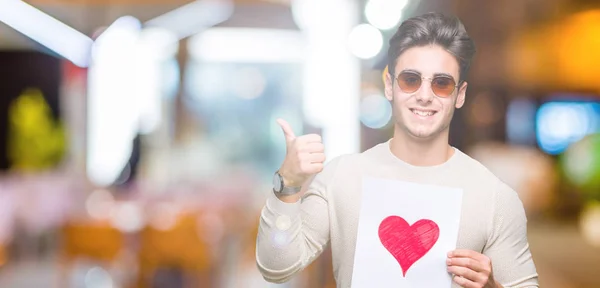 Joven Hombre Guapo Sosteniendo Tarjeta Con Corazón Rojo Sobre Fondo — Foto de Stock