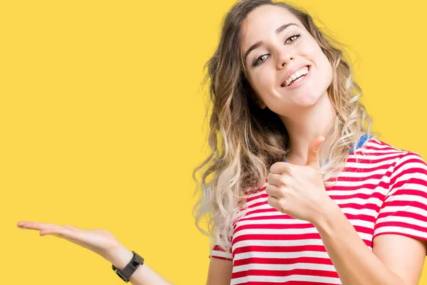 Beautiful young blonde woman over isolated background Showing palm hand and doing ok gesture with thumbs up, smiling happy and cheerful