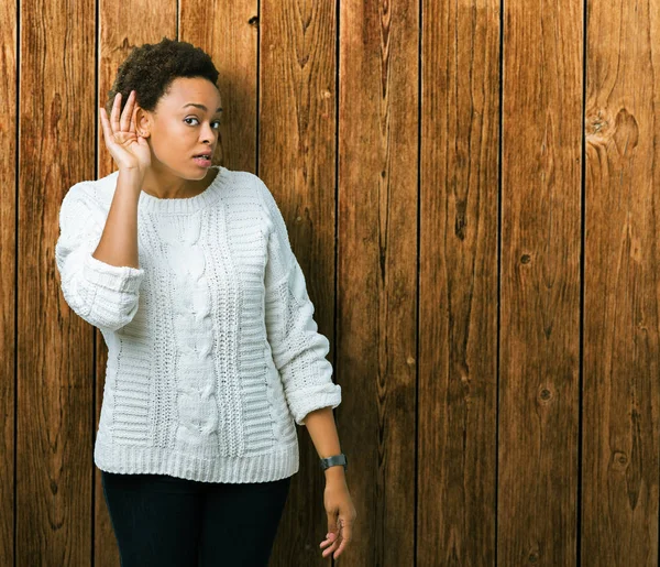 Beautiful young african american woman wearing sweater over isolated background smiling with hand over ear listening an hearing to rumor or gossip. Deafness concept.