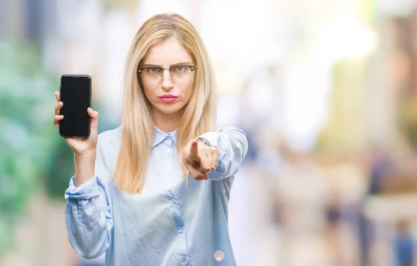 Young beautiful blonde business woman showing screen of smartphone over isolated background pointing with finger to the camera and to you, hand sign, positive and confident gesture from the front