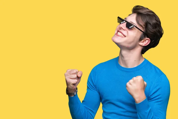 Young man wearing funny thug life glasses over isolated background very happy and excited doing winner gesture with arms raised, smiling and screaming for success. Celebration concept.