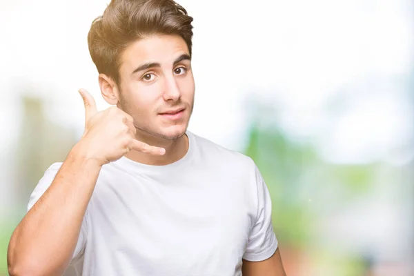 年轻英俊的男子穿着白色 T恤在孤立的背景微笑做电话手势用手和手指喜欢说话的电话 沟通概念 — 图库照片