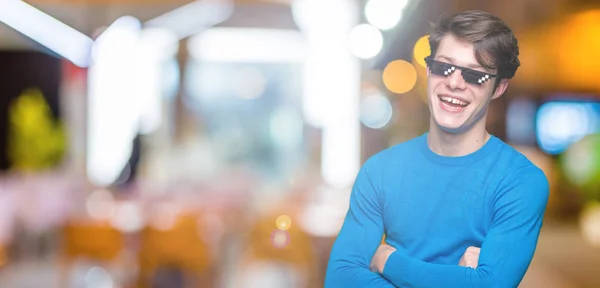 Young man wearing funny thug life glasses over isolated background happy face smiling with crossed arms looking at the camera. Positive person.