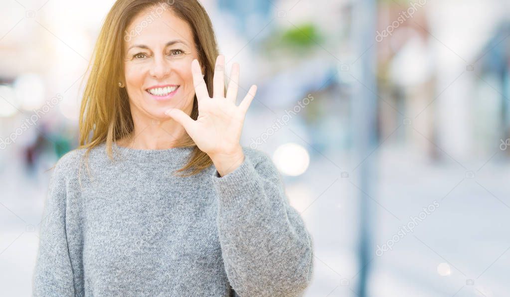 Beautiful middle age woman wearing winter sweater over isolated background showing and pointing up with fingers number five while smiling confident and happy.