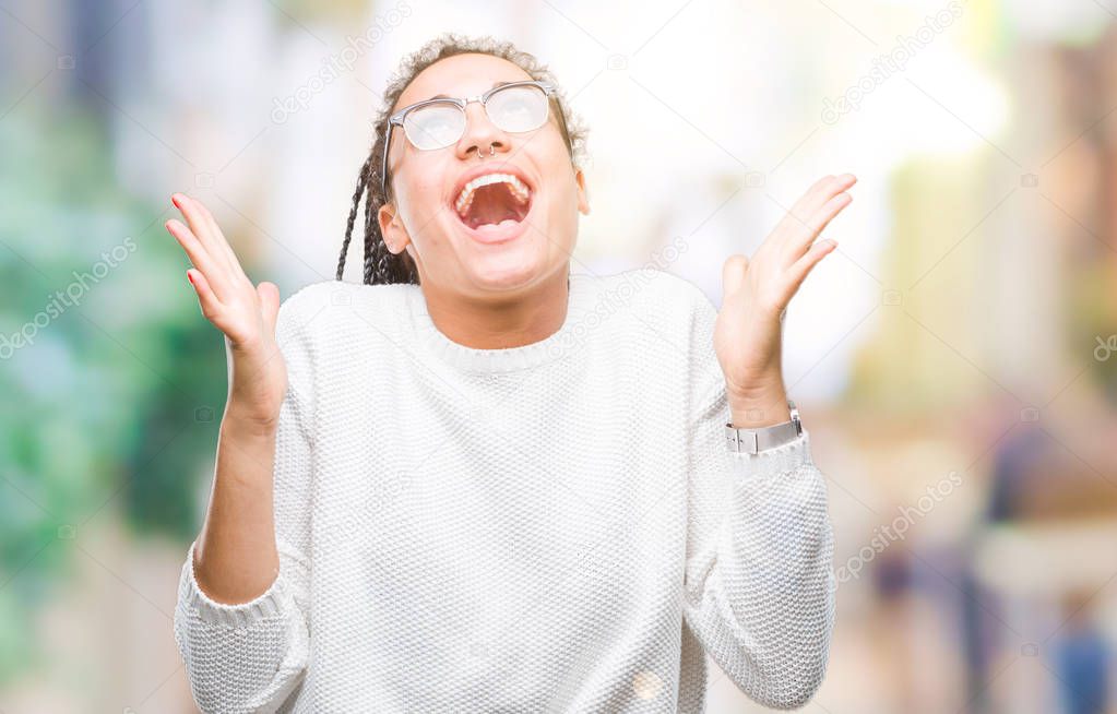 Young braided hair african american girl wearing glasses and sweater over isolated background celebrating crazy and amazed for success with arms raised and open eyes screaming excited. Winner concept