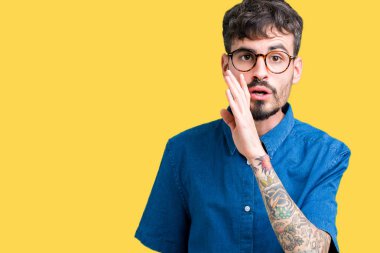 Genç yakışıklı adam gözlük izole arka plan üzerinde kötü amaçlı konuşma konuşma fısıldayan gizli söylenti söylüyor dudaklarından el