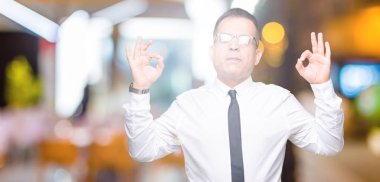 Orta yaş bussines Arap adam gözlük izole arka plan üzerinde dinlenmek ve gülümseyen gözlerle kapalı parmak jestle meditasyon yapıyor. Yoga kavramı.