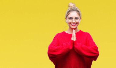 Kırmızı kazak ve gözlük ellerle birlikte AF emin gülümseyen için soran izole arka plan dua üzerinde giyen genç güzel sarışın kadın.