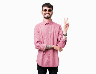 Genç yakışıklı adam mutlu yüz zafer işareti yaparken kameraya göz kırpıyor ile gülümseyen izole arka plan üzerinde güneş gözlüğü takıyor. İki numaralı.