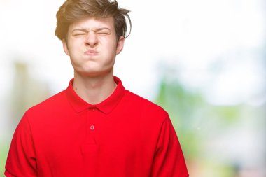 Komik surat ile yanakları şişirme izole arka plan üzerinde kırmızı t-shirt giyen genç yakışıklı adam. Ağız ile hava, deli ifade şişirilmiş.