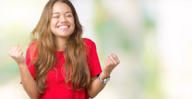 Genç güzel esmer kadın kutluyor izole arka plan üzerinde kırmızı t-shirt giyen şaşırttı ve silah ile başarı için yükseltilmiş ve açık gözler hayrete düşürdü. Kazanan kavramı.