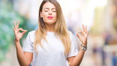 Genç güzel kadın rahat beyaz t-shirt izole arka plan üzerine dinlenmek ve gülümseyen gözlerle parmak ile meditasyon jest yapıyor kapalı. Yoga kavramı.