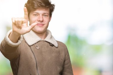 Gösterilen arka plan üzerinde kış ceket giyen genç yakışıklı adam izole ve parmakları ile işaret kendinden emin ve mutlu gülümseyerek ise ikinci.