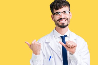 Arka plan üzerinde beyaz önlük giyen genç profesyonel bilim adam izole emin gülümseyen arkasından el ve kadar başparmak ile işaret