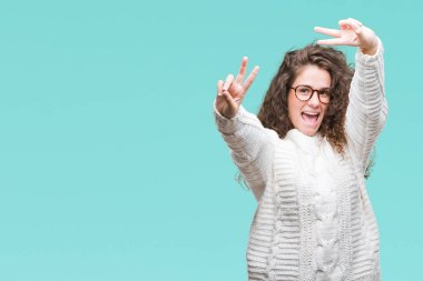 Güzel esmer kıvırcık saçlı Genç kız zafer işareti yapıyor parmak gösterilen kamera seyir gülümseyen izole arka plan üzerinde kış kazak giyiyor. İki numaralı.