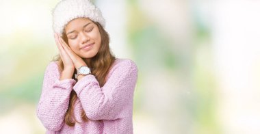 Genç güzel esmer kadın kazak ve kış şapka giyen izole arka plan uyuyan yorgun hayal ve el ile poz kapalı gözleri ile gülümseyen iken.