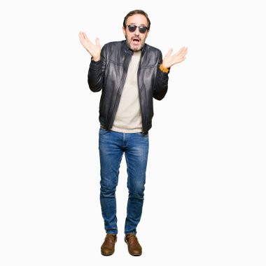Güneş gözlüğü ve siyah deri ceket clueless ve şaşkın bir ifadeyle kollar ve eller kaldırdı giyen orta yaş yakışıklı adam. Şüphe kavramı.