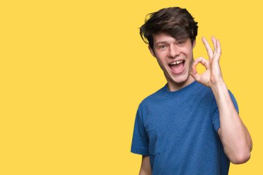 İzole arka plan el ve parmaklar ok işaretiyle yapıyor olumlu gülümseyen üzerinde mavi t-shirt giyen genç yakışıklı adam. Başarılı ifade.