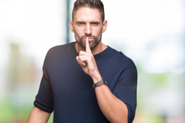 Dudaklarında parmak ile sessiz olmanı izole arka plan üzerinde kazak giyen genç yakışıklı adam. Sessizlik ve gizli kavramı.