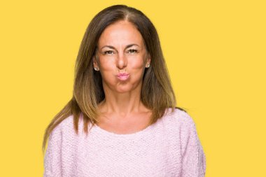 Komik surat ile yanakları şişirme izole arka plan üzerinde kış kazak giyen güzel orta yaş yetişkin kadın. Ağız ile hava, deli ifade şişirilmiş.