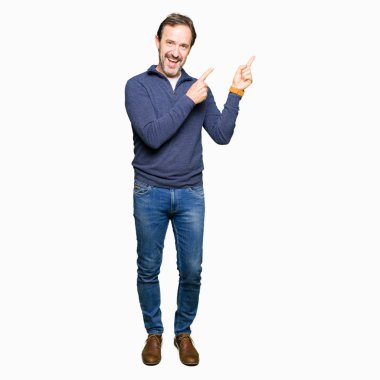 Gülümseyen ve iki elleri ve parmakları ile tarafına işaret kamera bakarak bir kazak giyen orta yaş yakışıklı adam.