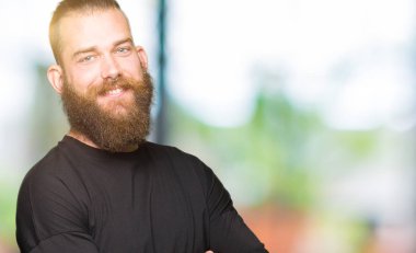 Rahat t-shirt mutlu yüz ile gülümseyen giyen genç sarışın adam kameraya seyir silah geçti. Olumlu bir kişi.