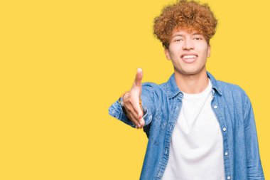 Afro saçlı kot giyen genç yakışıklı adam tebrik ve davet edici olarak gülümseyen dostu sunan karşılıklı ceket. Başarılı iş.