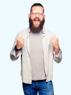 Gülümseyen ve başarı için çığlık çok mutlu ve heyecanlı kaldırdı, silah ile kazanan jest yapıyor gözlüklü genç sarışın adam. Kutlama kavramı.