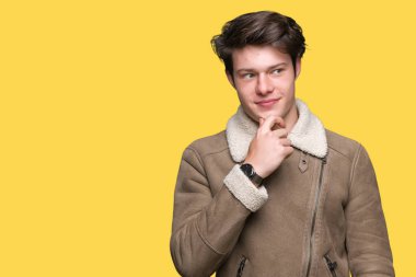 Genç yakışıklı adam emin çapraz kollar ve çeneme kaldırdı el ile gülümseme ile kameraya bakarak izole arka plan üzerinde kış palto giyiyor. Pozitif düşünce.