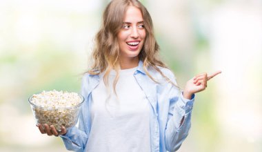 İzole arka tarafına el ve parmak ile işaret çok mutlu üzerinde patlamış mısır yemek güzel sarışın genç kadın