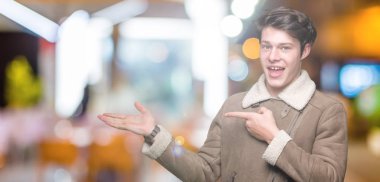 Hayret ve el ile sunulması ve parmak ile işaret ederken kameraya gülümseyen izole arka plan üzerinde kış ceket giyen genç yakışıklı adam.