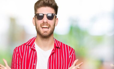 Çılgın kutlama giyen güneş gözlüğü genç yakışıklı adam ve silah ile başarı için hayran çığlık kaldırdı ve açık gözleri heyecanlı. Kazanan kavramı