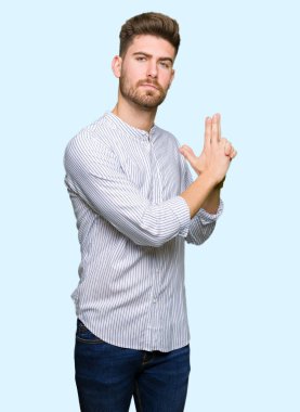 Genç yakışıklı bir adam sembolik bir silah tutuyor. El hareketleriyle cinayet silahlarıyla oynuyor. Kızgın surat.