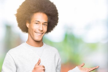 Sportif kazak gösteren palm el giyen ve yukarıya, mutlu ve neşeli gülümseyen baş parmakları Tamam jest yapıyor afro saçlı genç Afro-Amerikan adam