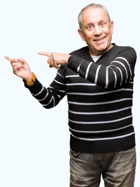 Gülümseyen ve iki el ve parmak tarafına işaret kamera bakarak kış çizgili kazak giyen yakışıklı kıdemli adam.