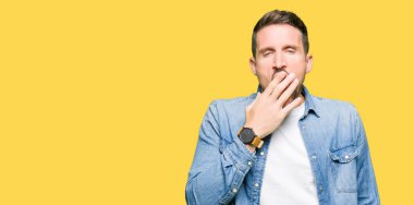 Yakışıklı adam mavi gözleri ve denim ceket giyen sakal esneme yorgun kapsayan ağız el ile sıkılmış. Restless ve uyku hali.