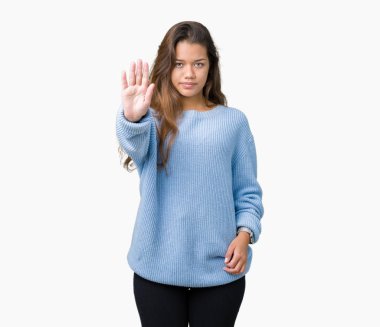 İzole arka plan üzerinde mavi kış kazak giyen genç güzel esmer kadın el avuç ile şarkı durdurmak yapıyor. Yüz üzerinde negatif ve ciddi jest ile uyarı ifadesi.