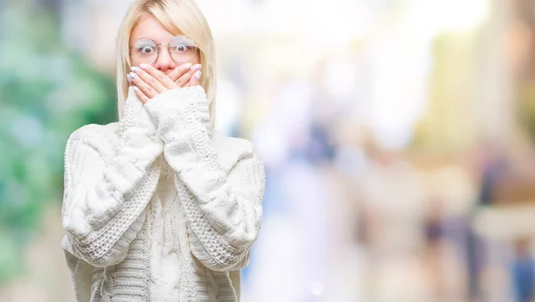 若い美しい金髪女性の孤立した背景のミスのための手で口を覆っているショックを受けた上冬のセーターとメガネを着用します 秘密の概念 — ストック写真